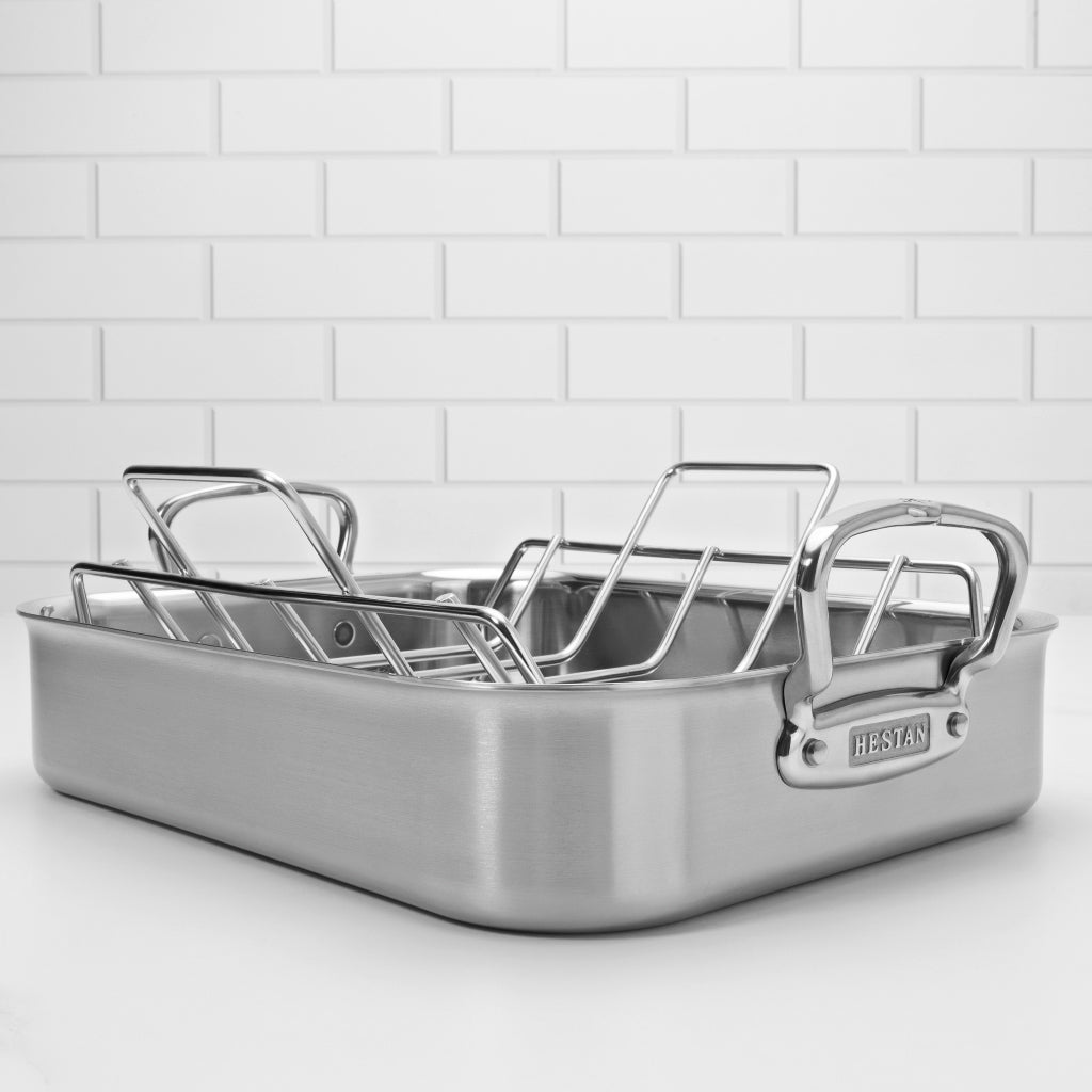 A large Hestan roasting pan sits on a white countertop in front of a white tile backsplash.