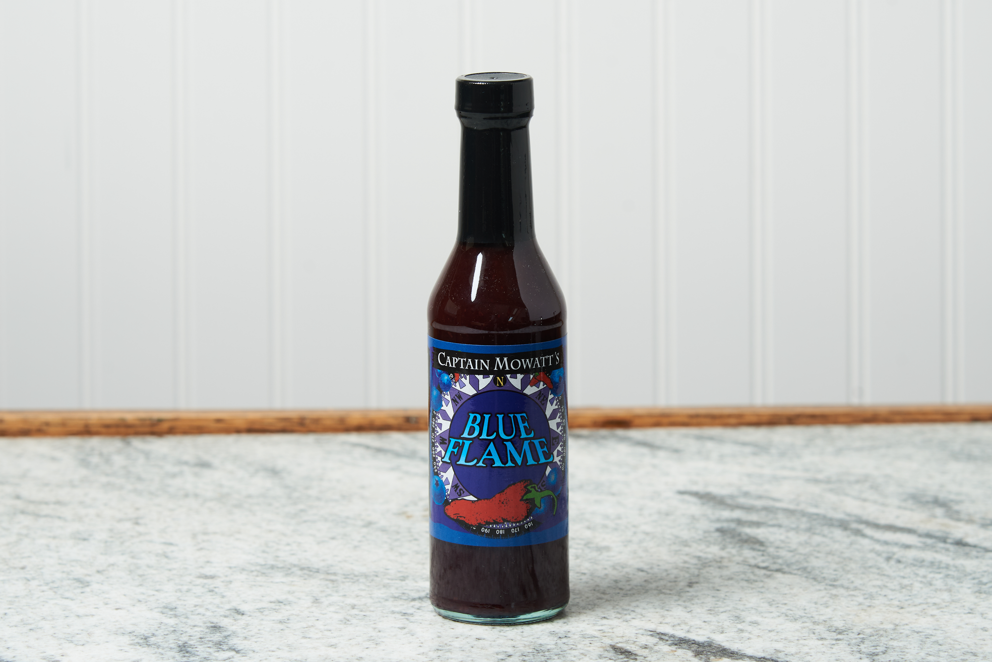 A bottle of Captain Mowatt's Blue Flame Sauce sits on a marble countertop.