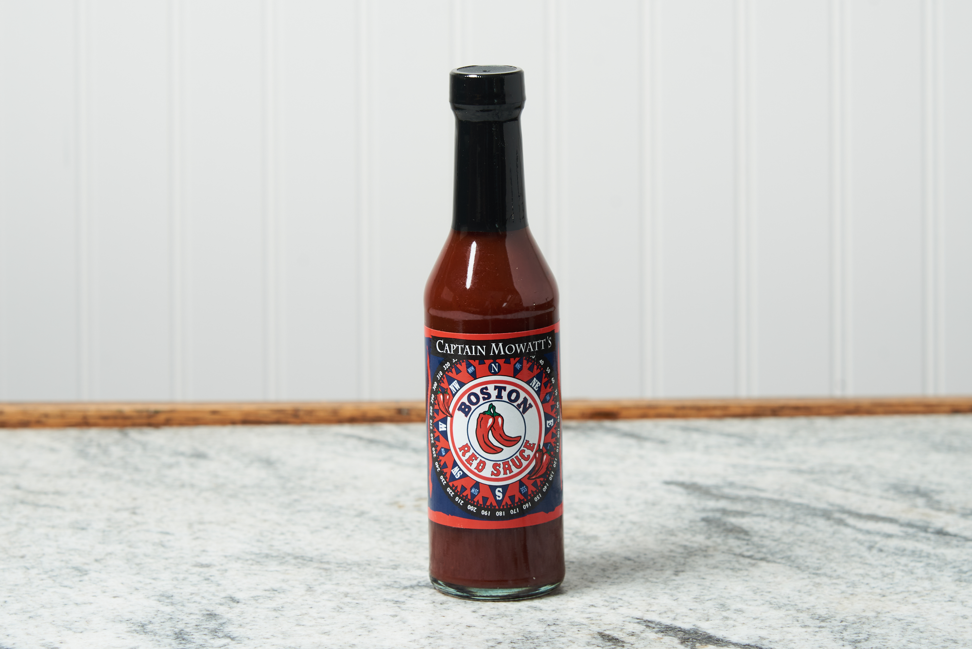 A bottle of Captain Mowatt's Boston Red Sauce sits on a marble countertop.