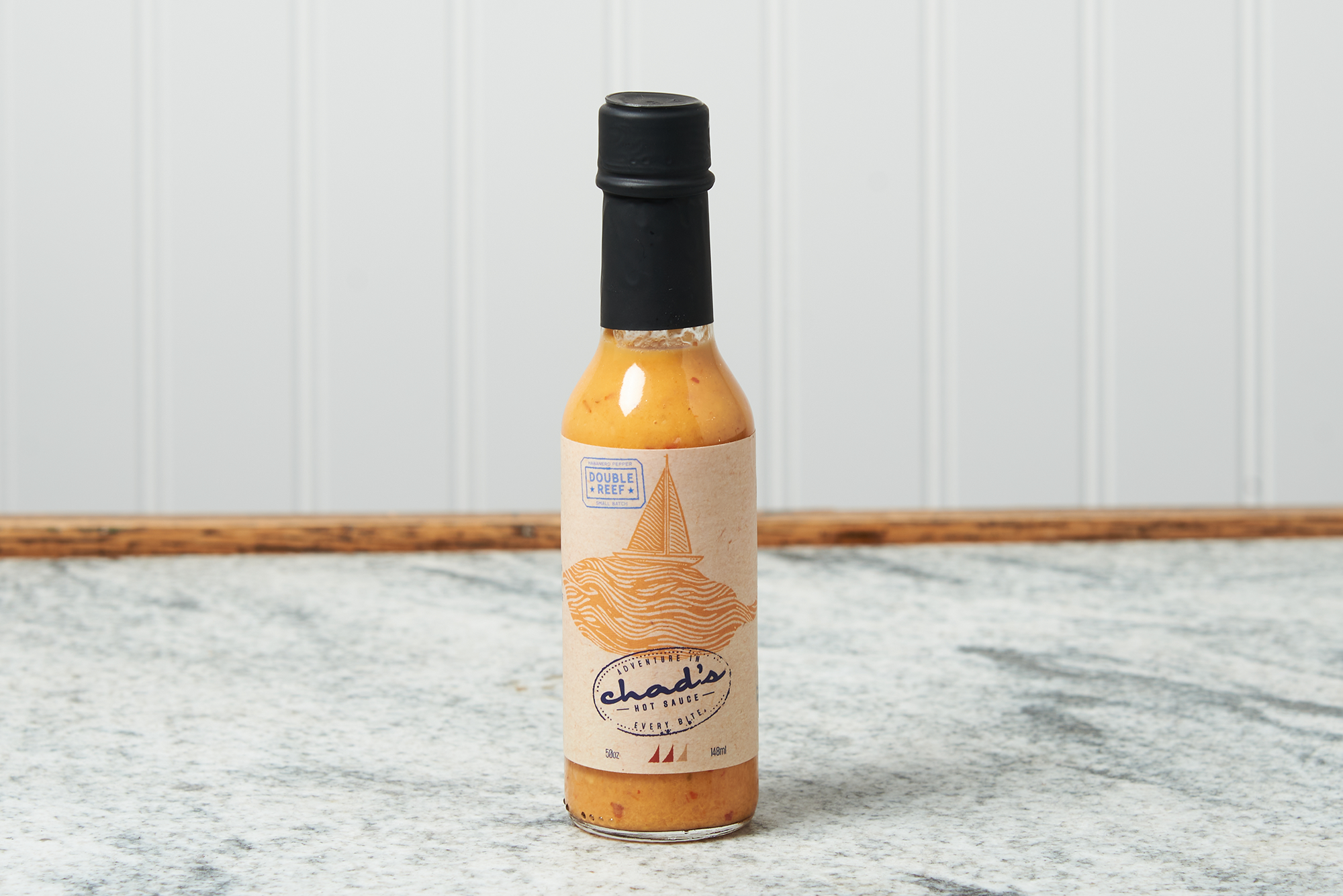 A bottle of Chad's Double Reef Hot Sauce sits on a marble countertop.