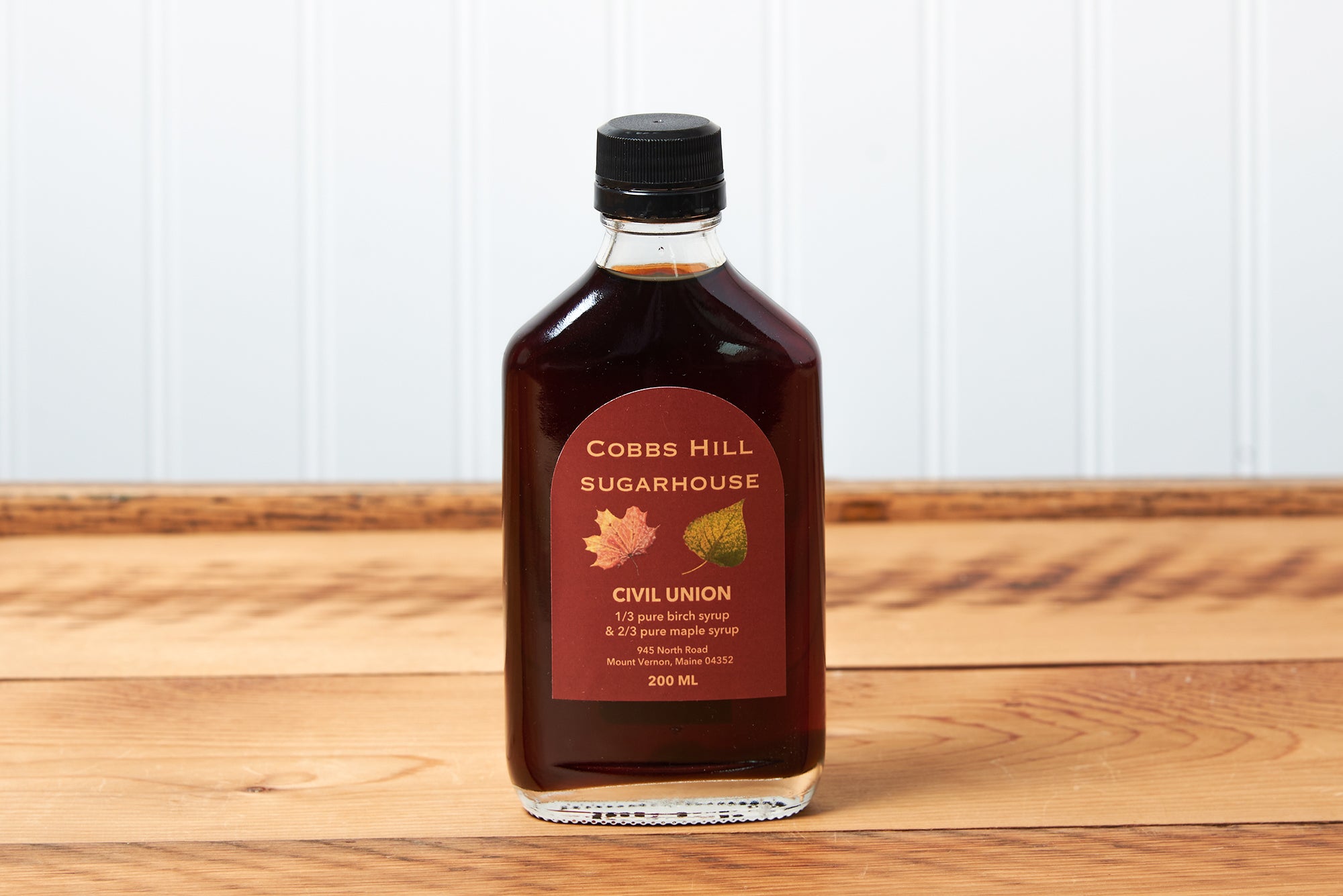 A bottle of Cobb's Hill Civil Union Maple Syrup sits on a brown wooden table.