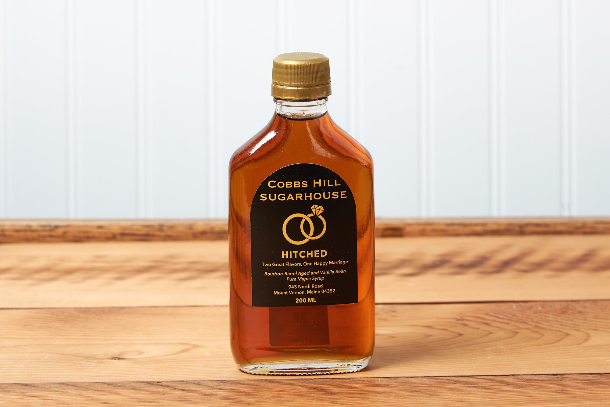 A bottle of Cobb's Hill Hitched Maple Syrup sits on a brown wooden table.