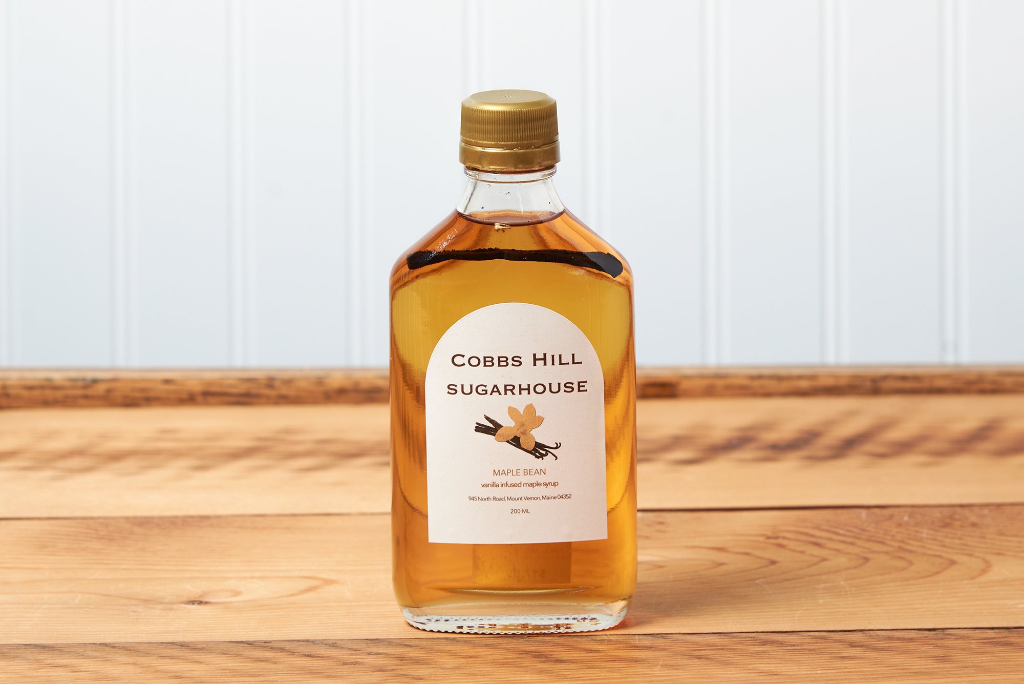 A bottle of Cobb's Hill Maple Bean Maple Syrup sits on a brown wooden table.