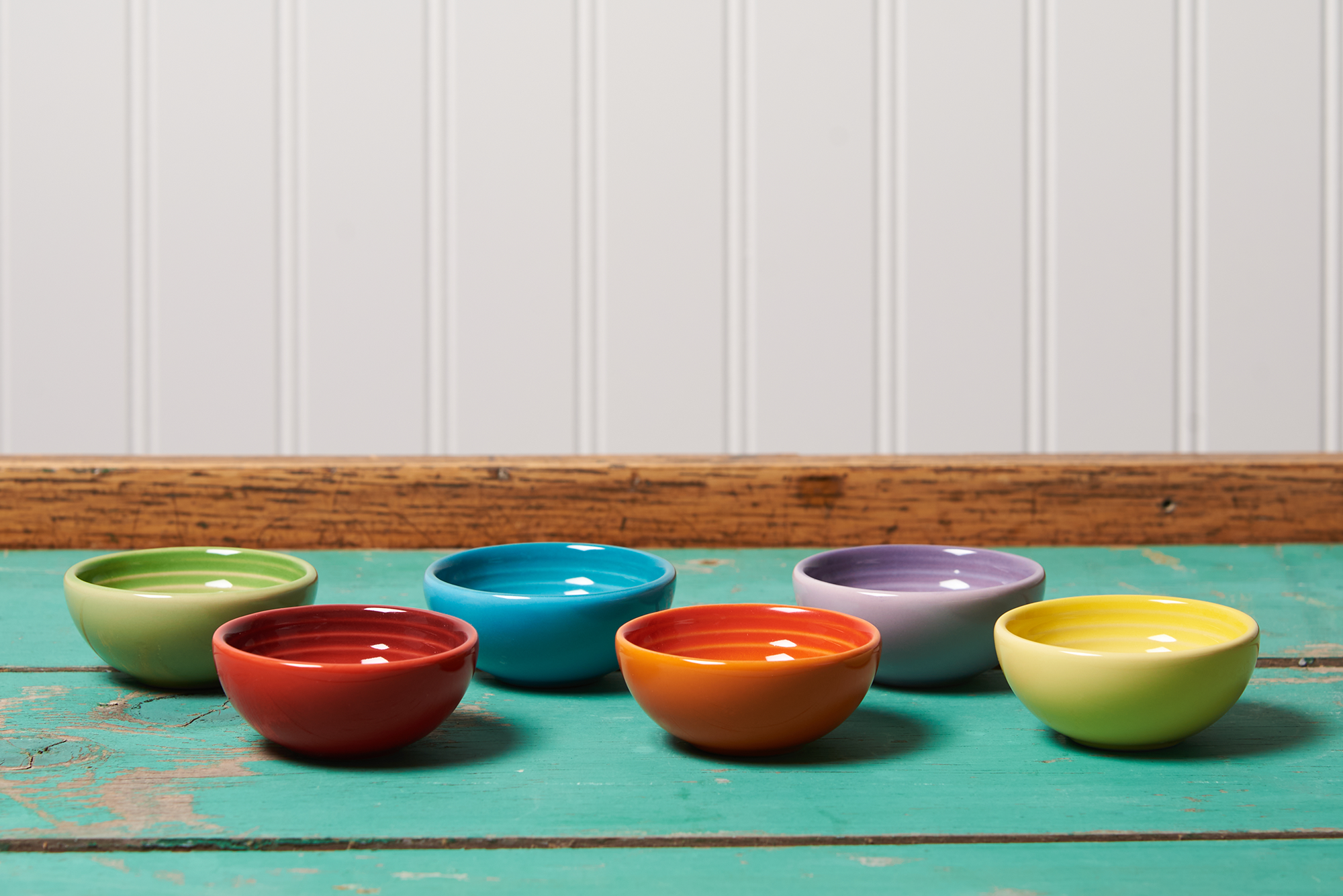 Six Le Creuset pinch bowls in assorted colors sit on a turquoise table.