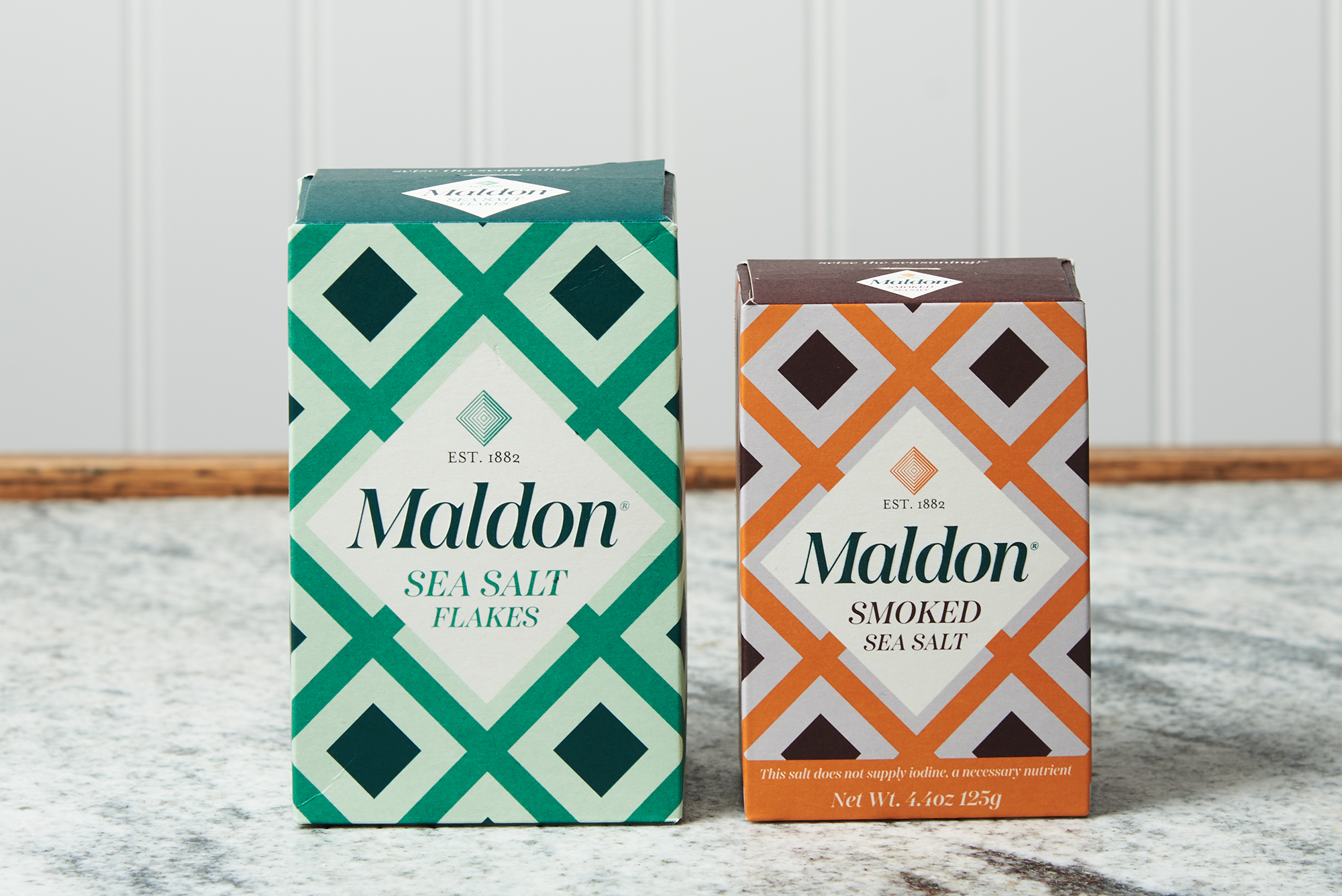 Two boxes of Maldon Sea Salt Flakes sit on a marble countertop. One box is classic Sea Salt Flakes, the other box is Smoked Sea Salt.