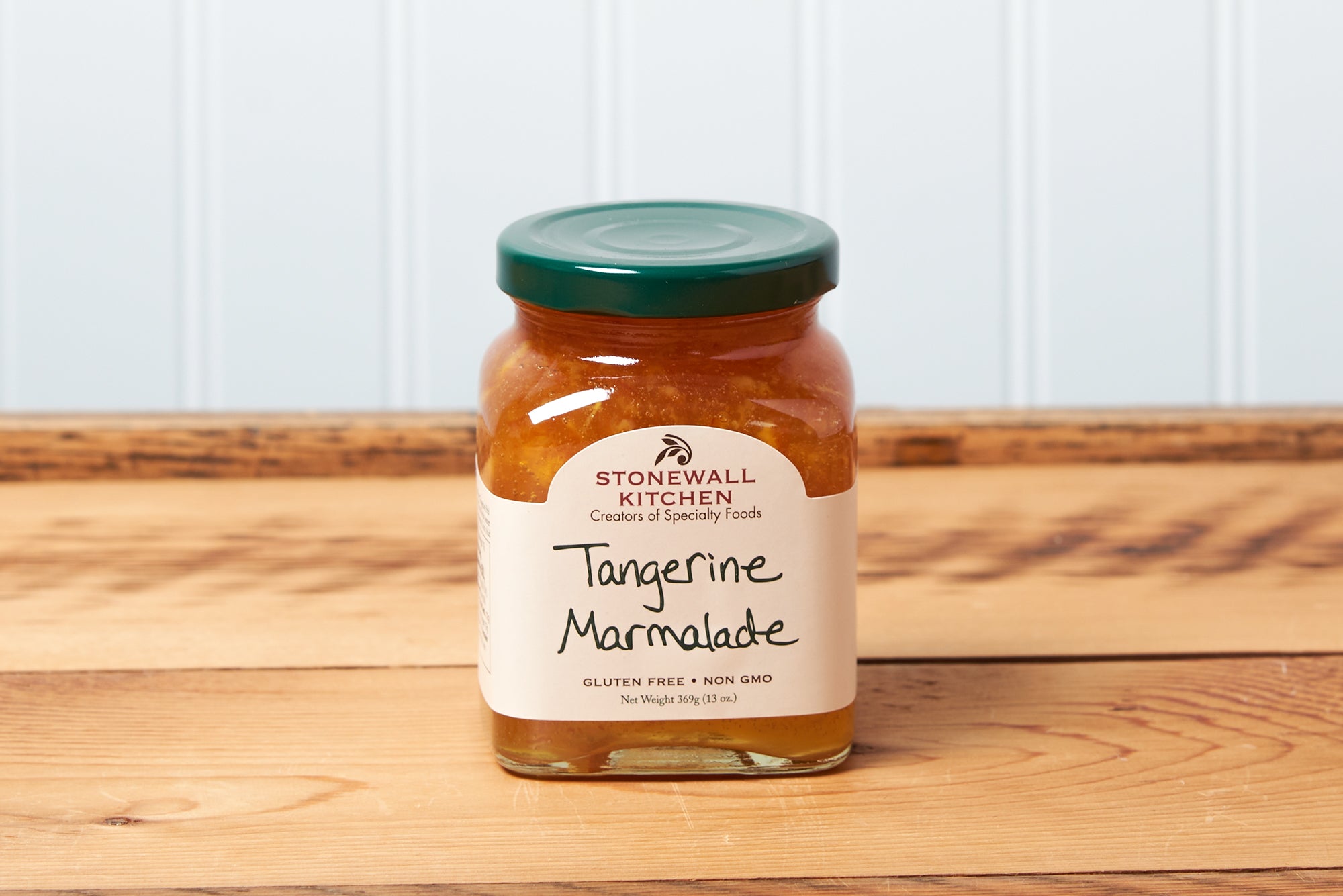 A jar of Stonewall Kitchen Tangerine Marmalade sits on a brown wooden table.