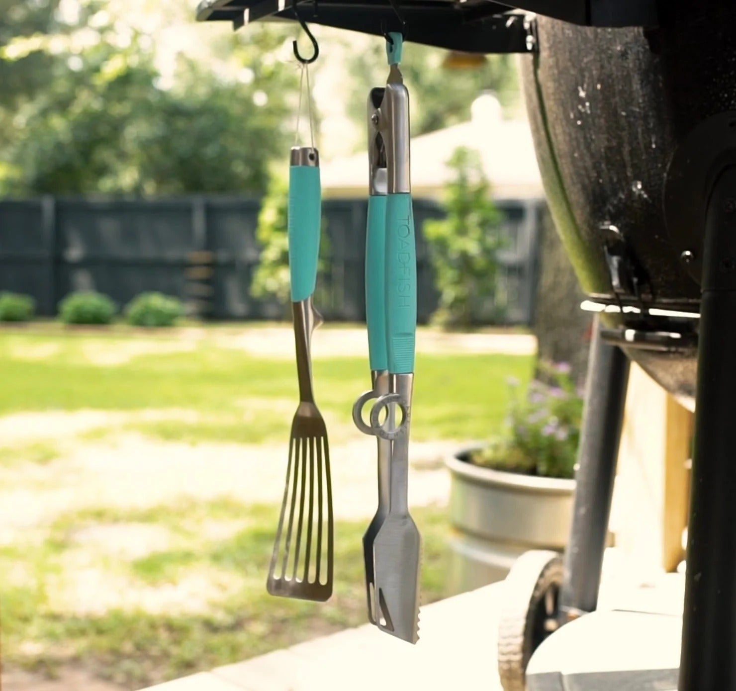 The Toadfish Ultimate Grill Set tools hang from a grill in a backyard.