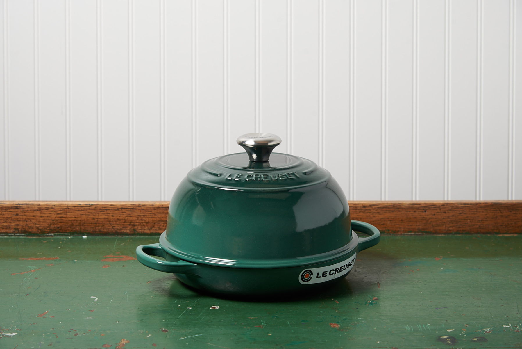 Green Le Creuset casserole dish on wooden table with white beadboard background
