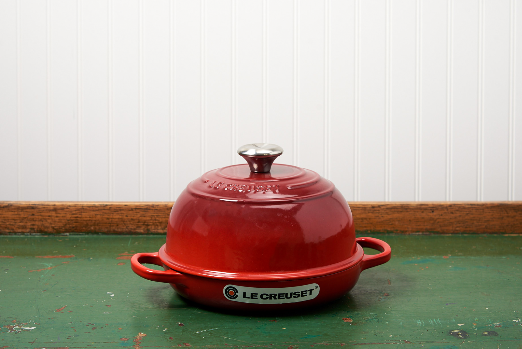 Red Le Creuset Dutch oven on worn green table against white beadboard background