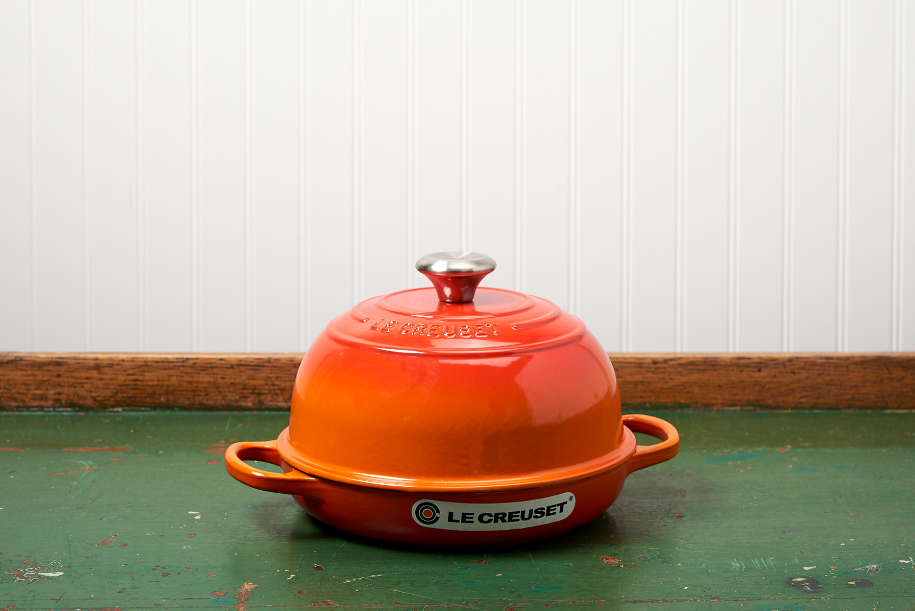 Orange Le Creuset Dutch oven on a rustic green table with a white backdrop.