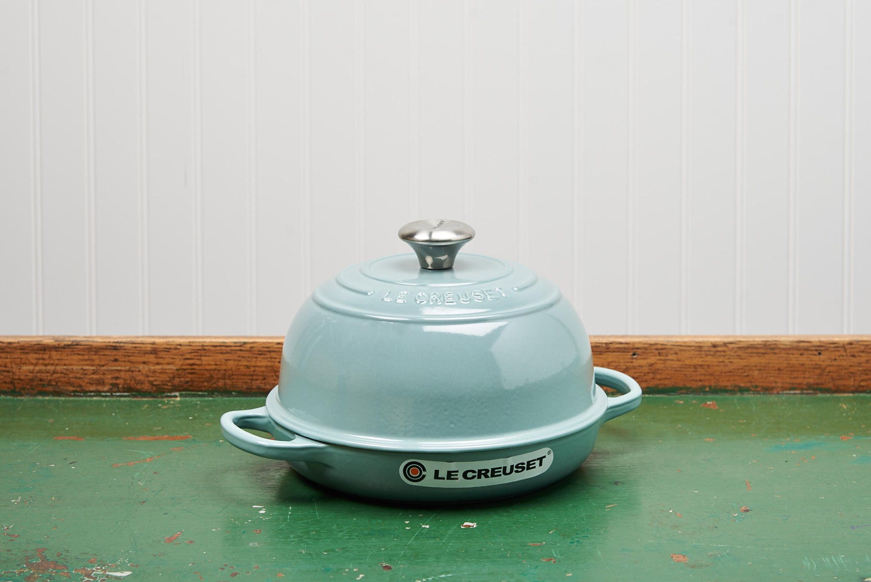 Mint green Le Creuset dutch oven on wooden table against white beadboard
