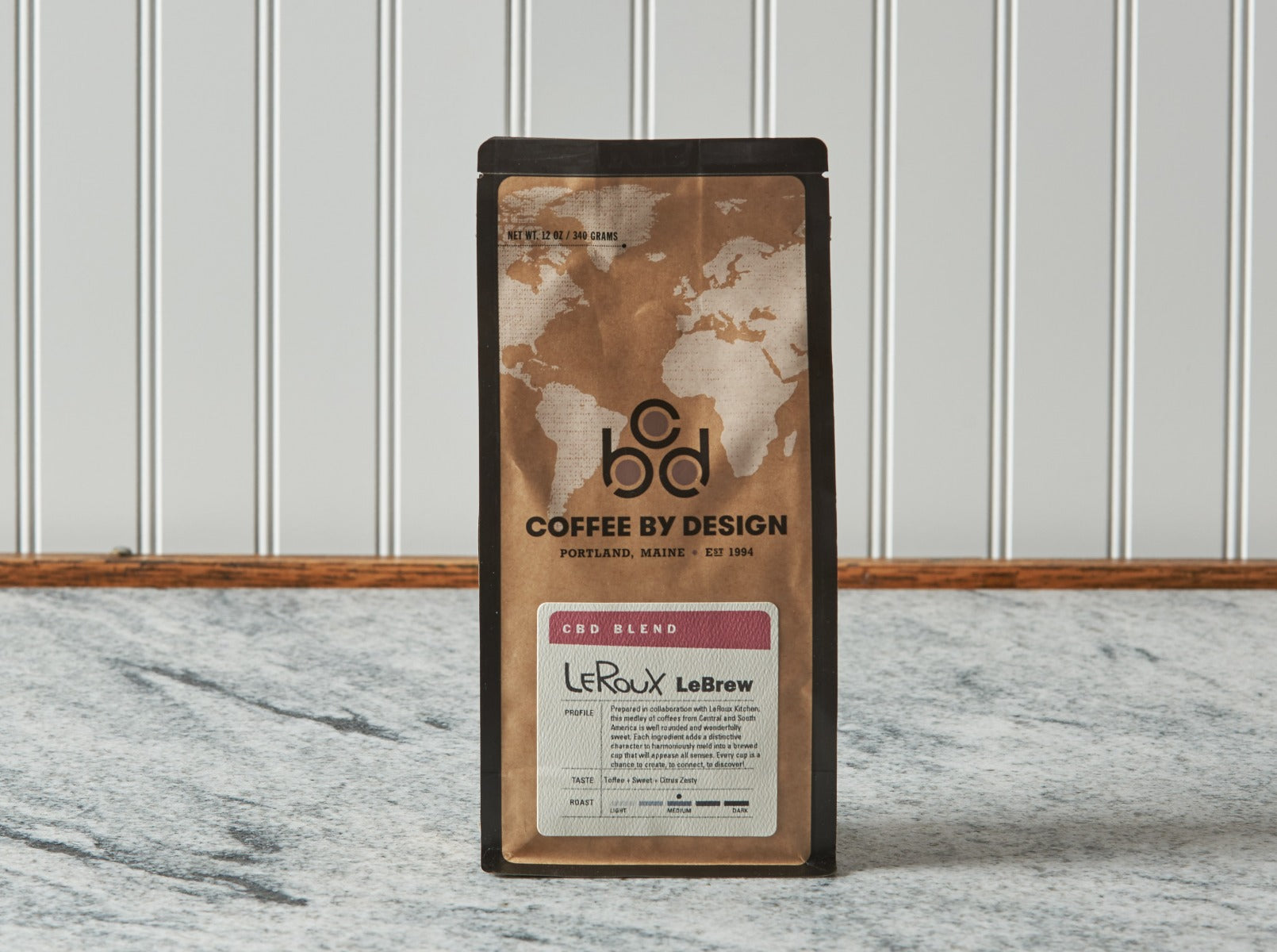 Coffee by Design bag on counter with world map design, branding, and CBD blend label.