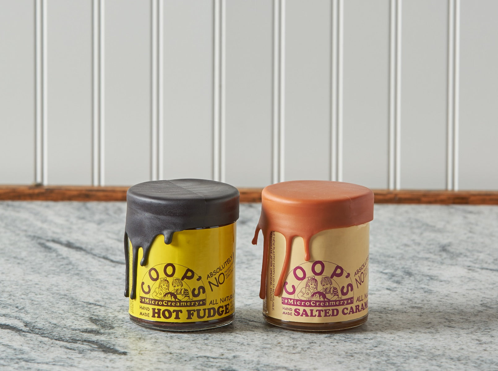 Two jars of Coop's hot fudge and salted caramel sauces on marble counter.
