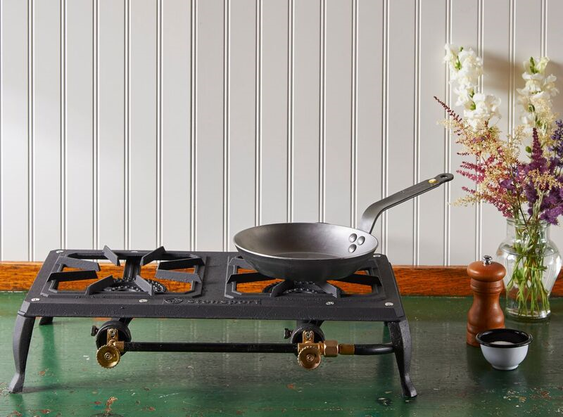 A Debuyer Mineral B Carbon Steel Fry Pan rests on a portable stovetop, which sits on a green table in front of a white wall.