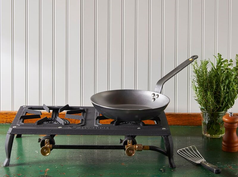 A Debuyer Mineral B Carbon Steel Fry Pan rests on a portable stovetop, which sits on a green table in front of a white wall.