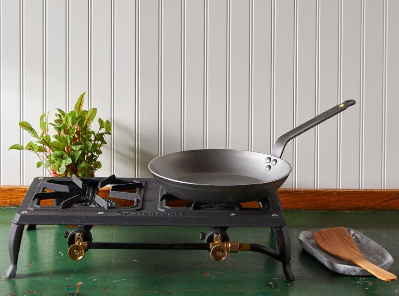 A Debuyer Mineral B Carbon Steel Fry Pan rests on a portable stovetop, which sits on a green table in front of a white wall.