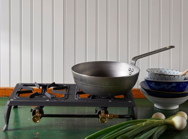 A Mineral B Carbon Steel Deep Fry Pan rests on a portable stovetop, which sits on a green table in front of a white wall.