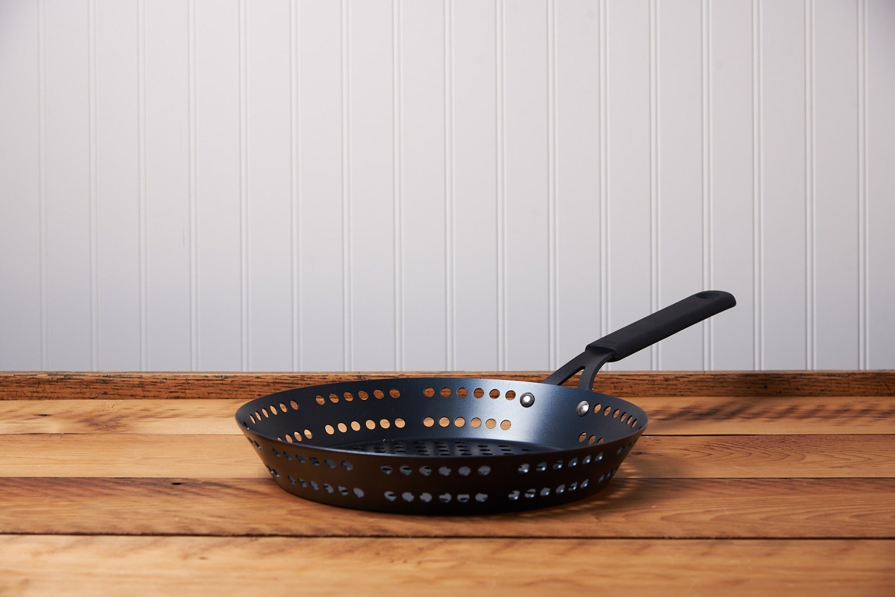 An OXO 12" Obsidian Outdoor Carbon Steel Frypan sits on a brown, wooden table.