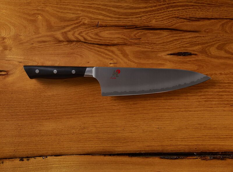 Chef's knife with serrated edge on wooden background
