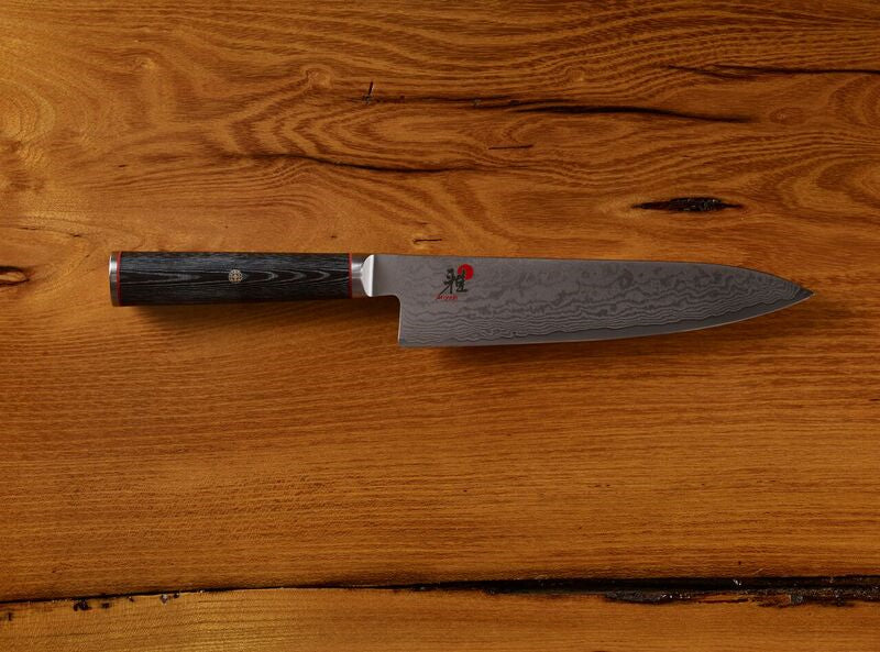 Damascus steel chef knife with dark handle on wooden background