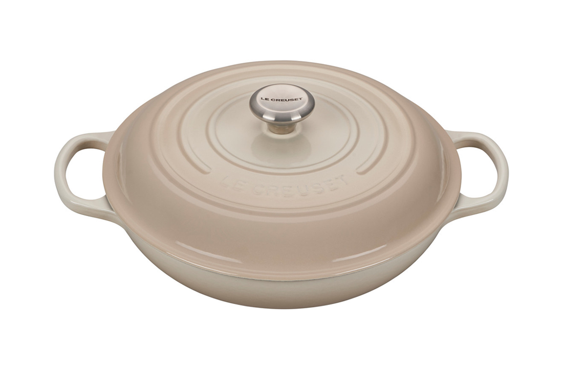 Beige Le Creuset cast iron dutch oven with lid on white background