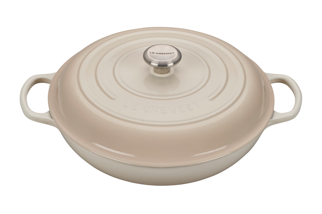 Beige enameled cast iron Dutch oven by Le Creuset on white background