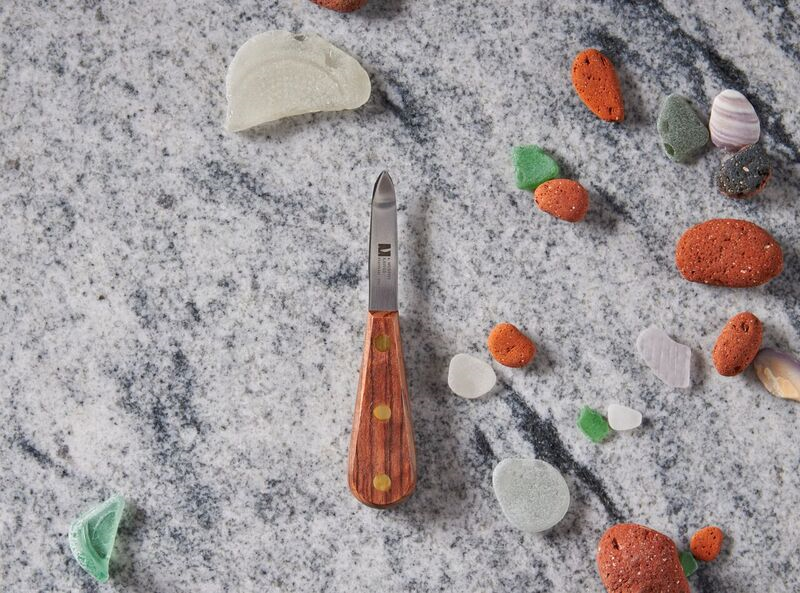 Pocket knife with wooden handle among colorful sea pebbles on marble surface