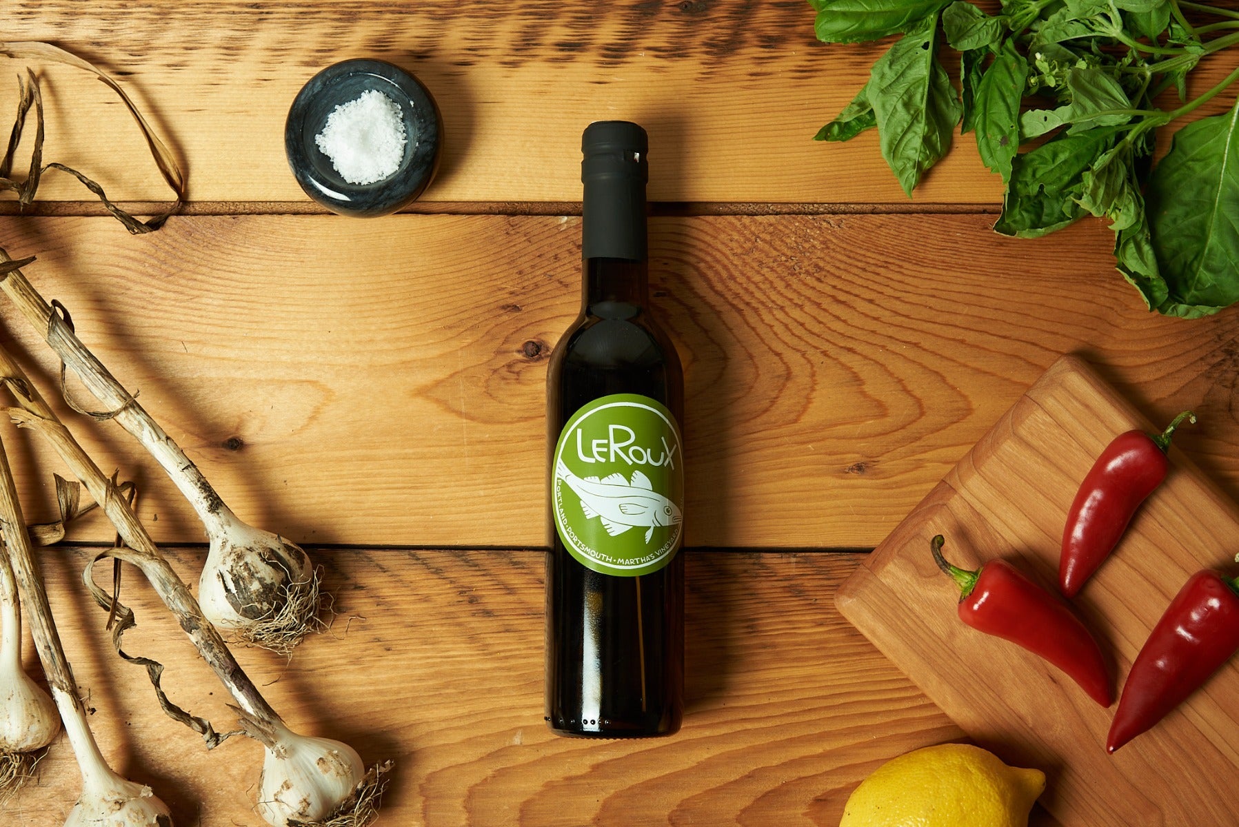 Organic olive oil bottle on wooden table with garlic, basil, lemon, and chili.