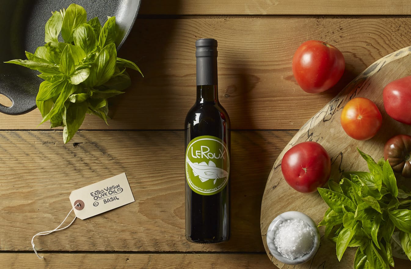 Bottle of LeRoux olive oil with fresh basil and ripe tomatoes on wooden table.
