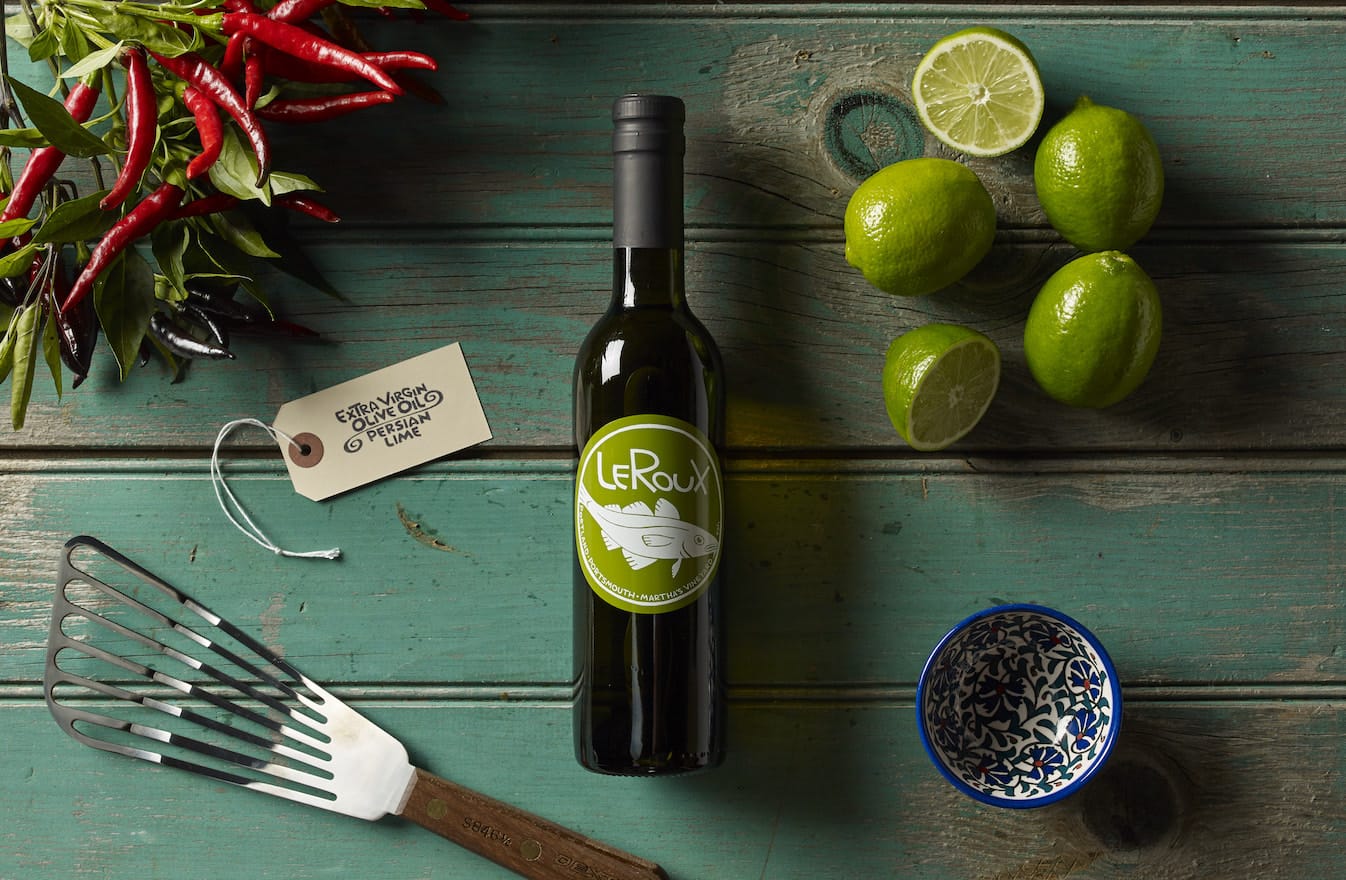 Wine bottle with limes, chili peppers, olive oil tag, and fork on wooden table