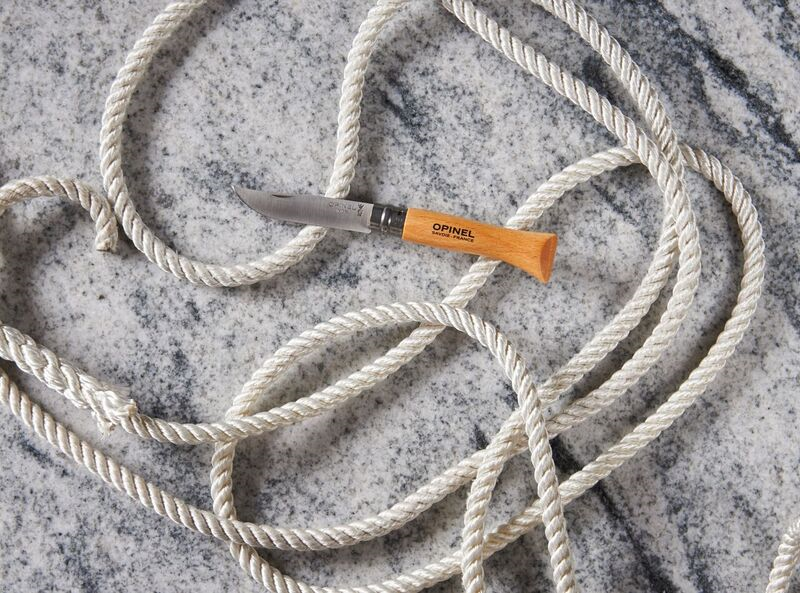 Coiled white rope and a pocket knife with wooden handle on marble surface