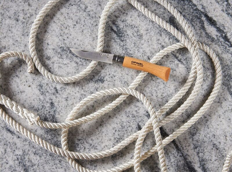 Opinel pocket knife on marble surface with white coiled rope.