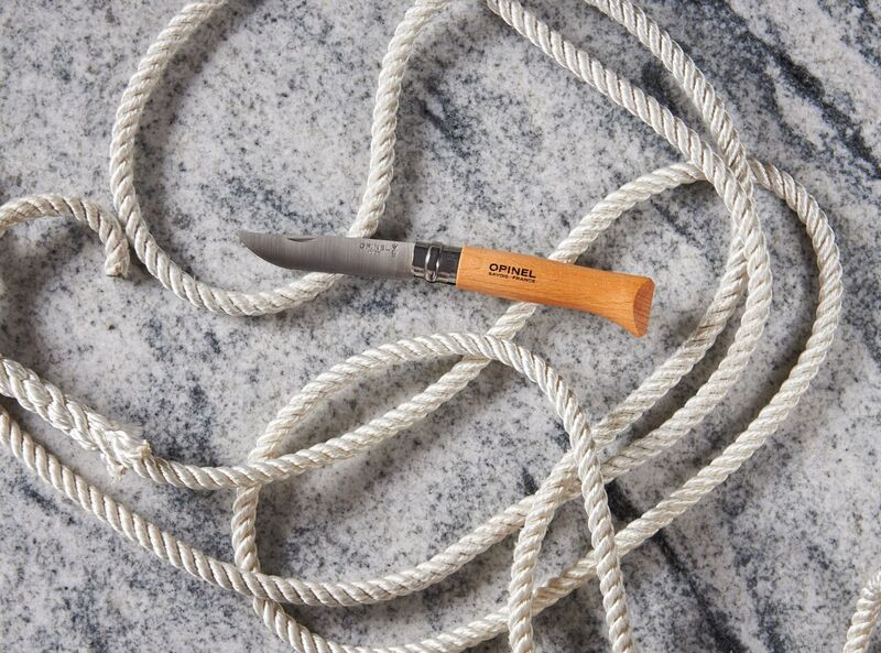 Pocket knife with wood handle on marble surface entwined with white rope.