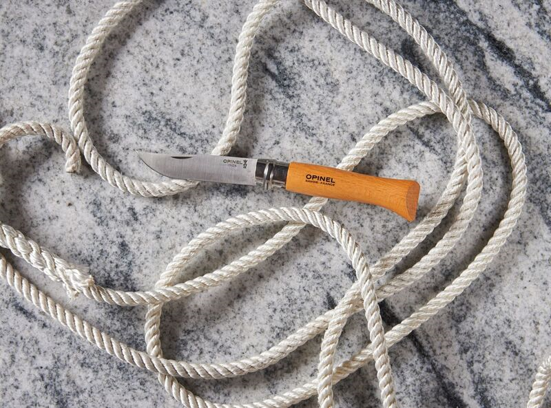 Opinel pocket knife with wooden handle on a coiled rope and marble background