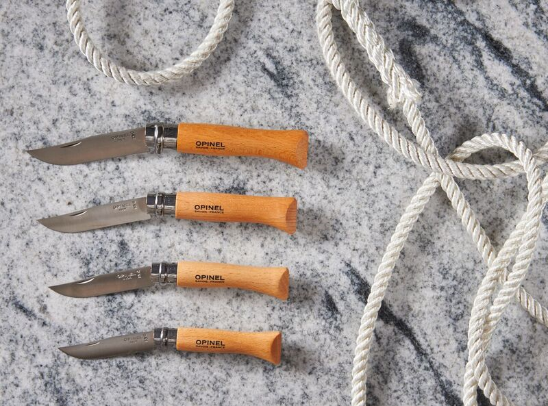 Four Opinel pocket knives with wooden handles next to a coiled rope on marble