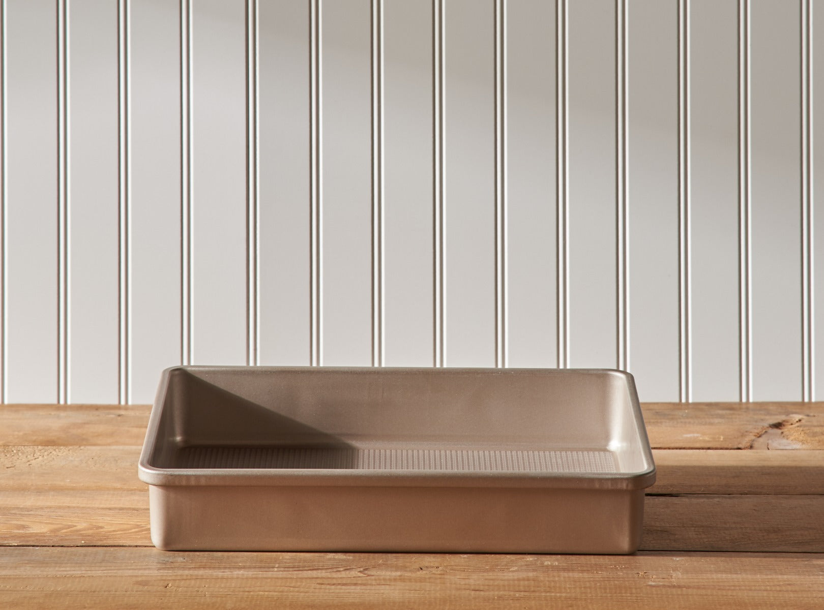 A 9"x13" OXO Cake Pan sits on a wooden table, in front of a white wall.