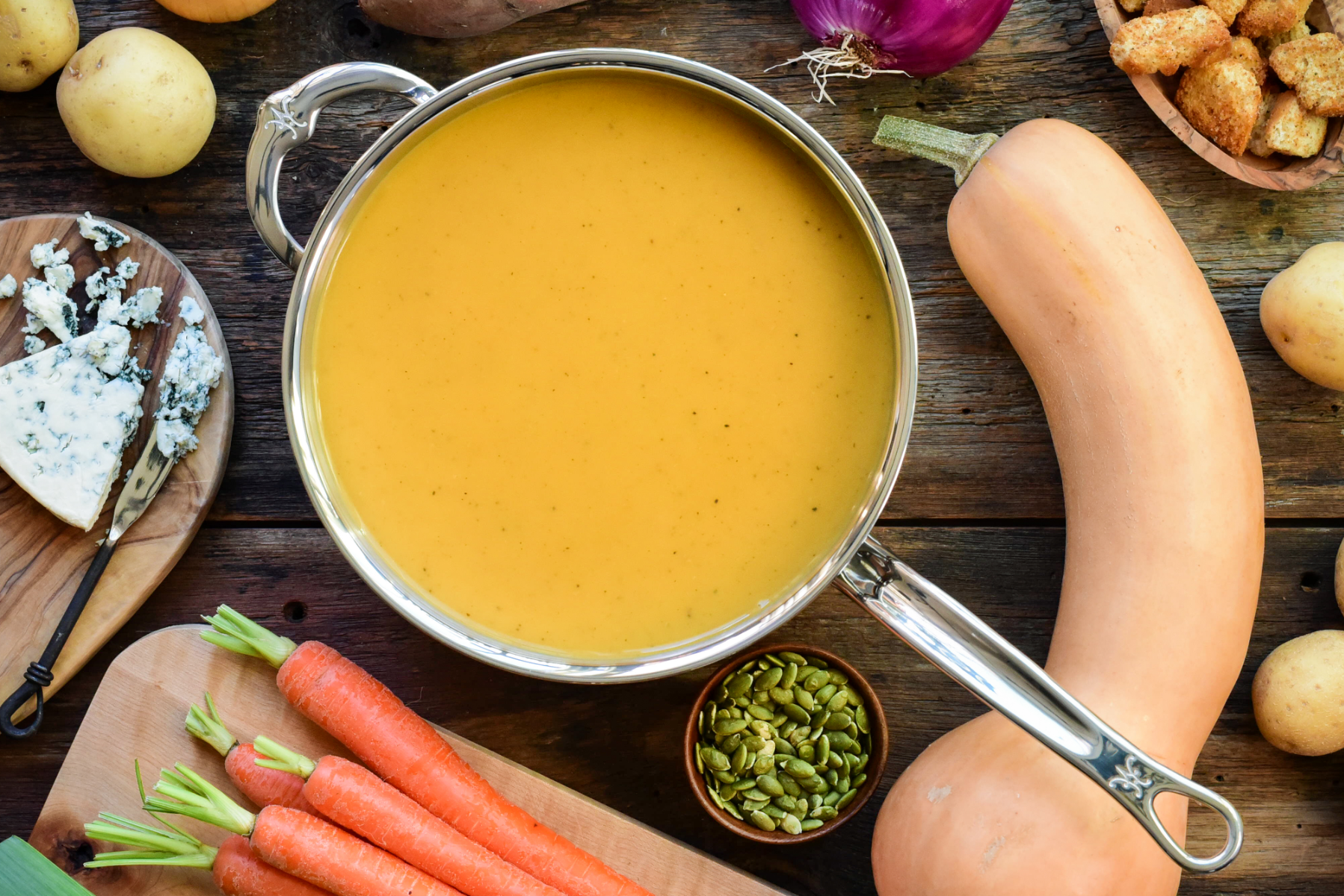 Homemade butternut squash soup in pot with fresh ingredients around