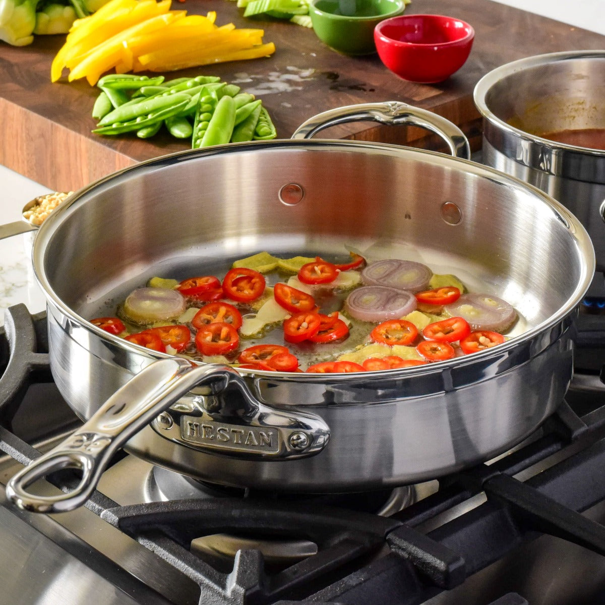 Stainless steel pot on stove with sliced chili and onions, prep vegetables in background