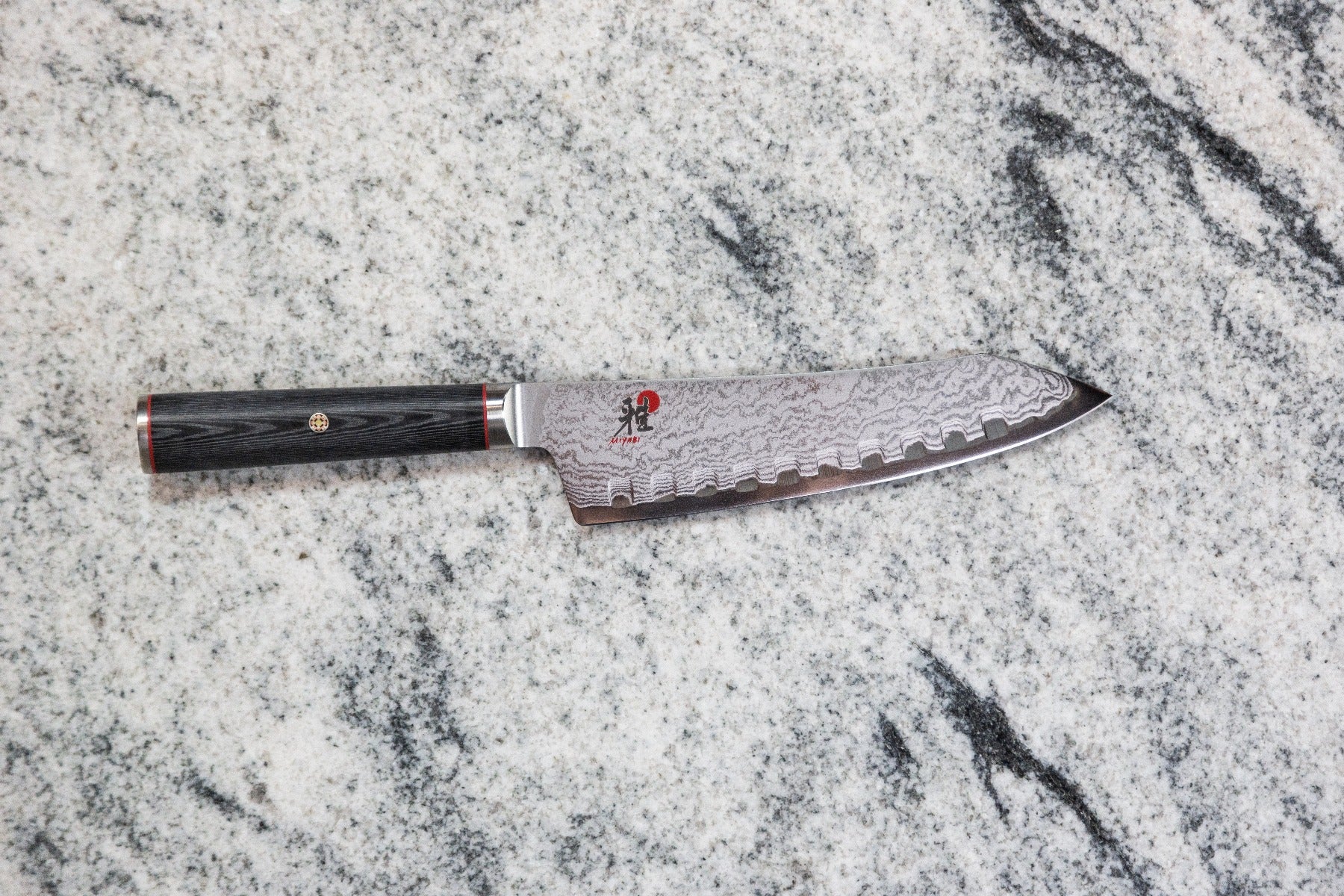 Damascus steel chef knife with serrated edge on marble background