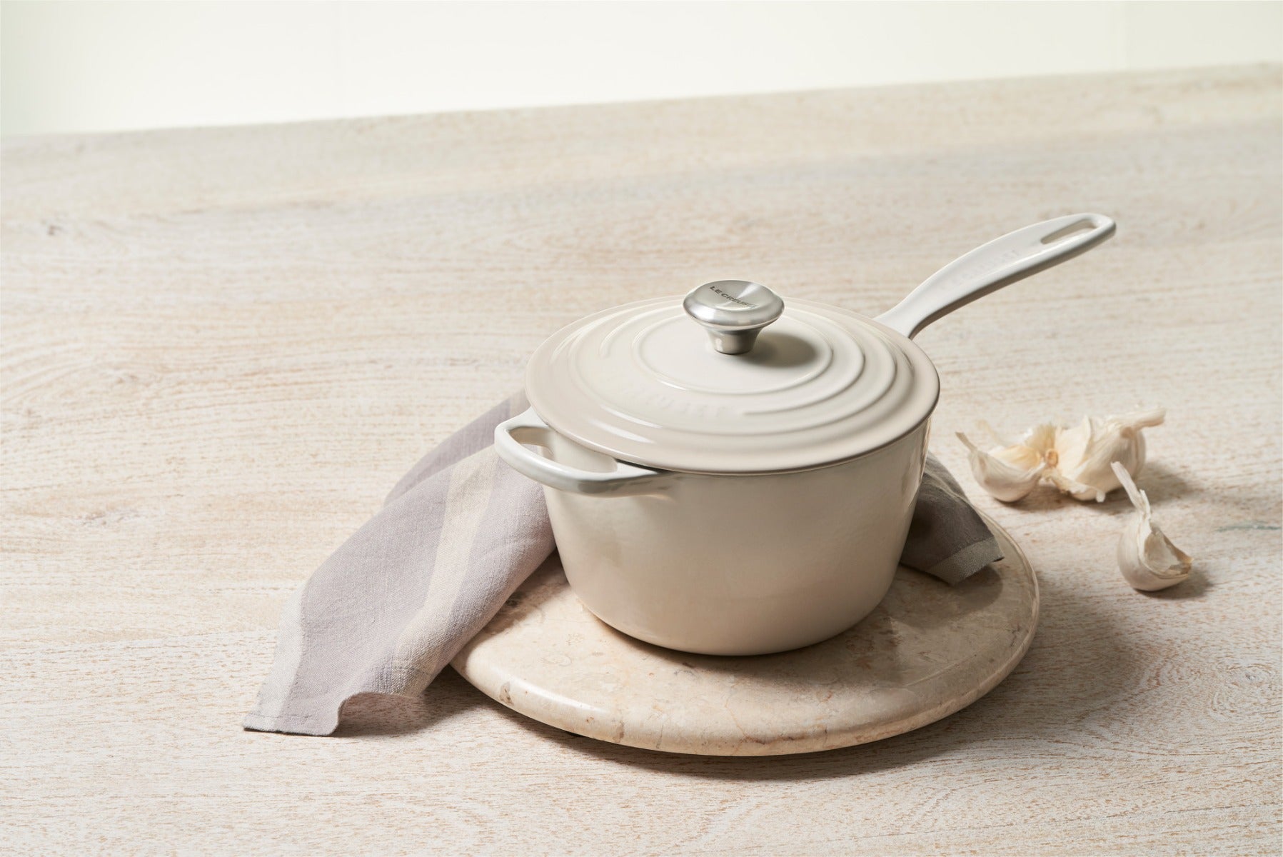 White enamel saucepan on a marble trivet with garlic cloves and cloth