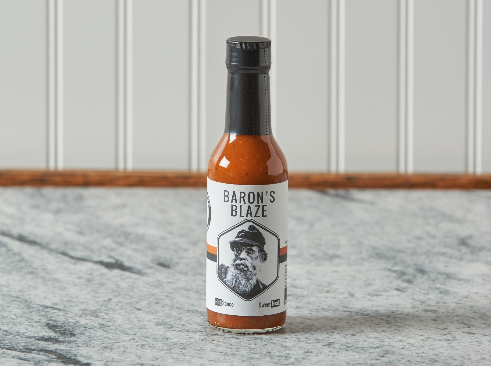 Baron's Blaze hot sauce bottle on marble countertop against striped wall