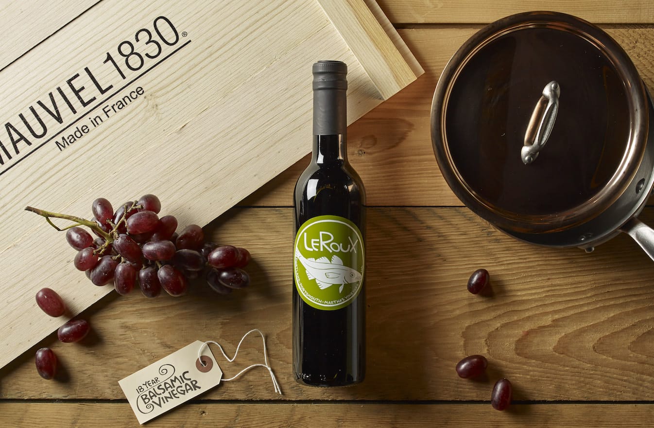 Wine bottle, fresh grapes, and quality cookware on a wooden table.