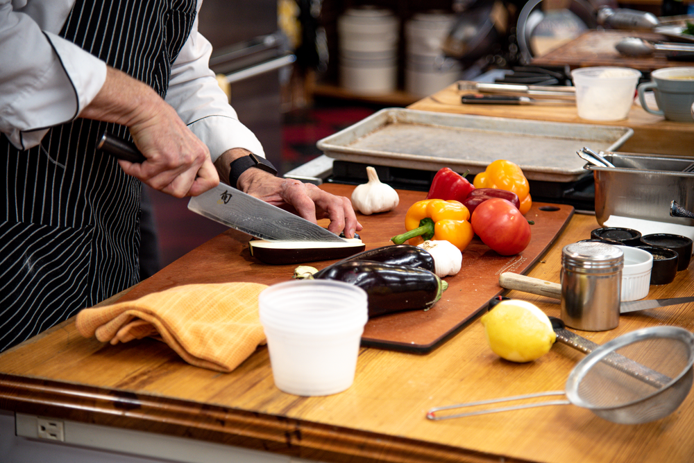 A chef chops assorted vegetables on a  cutting board.