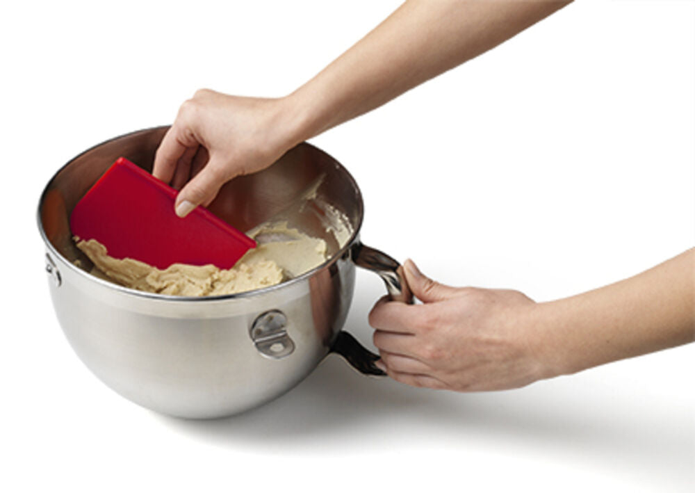 A red Chef'n Bench Scraper is used to scrap dough from a stainless steel bowl.