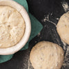 Fresh bread dough proofing in baskets on floured surface