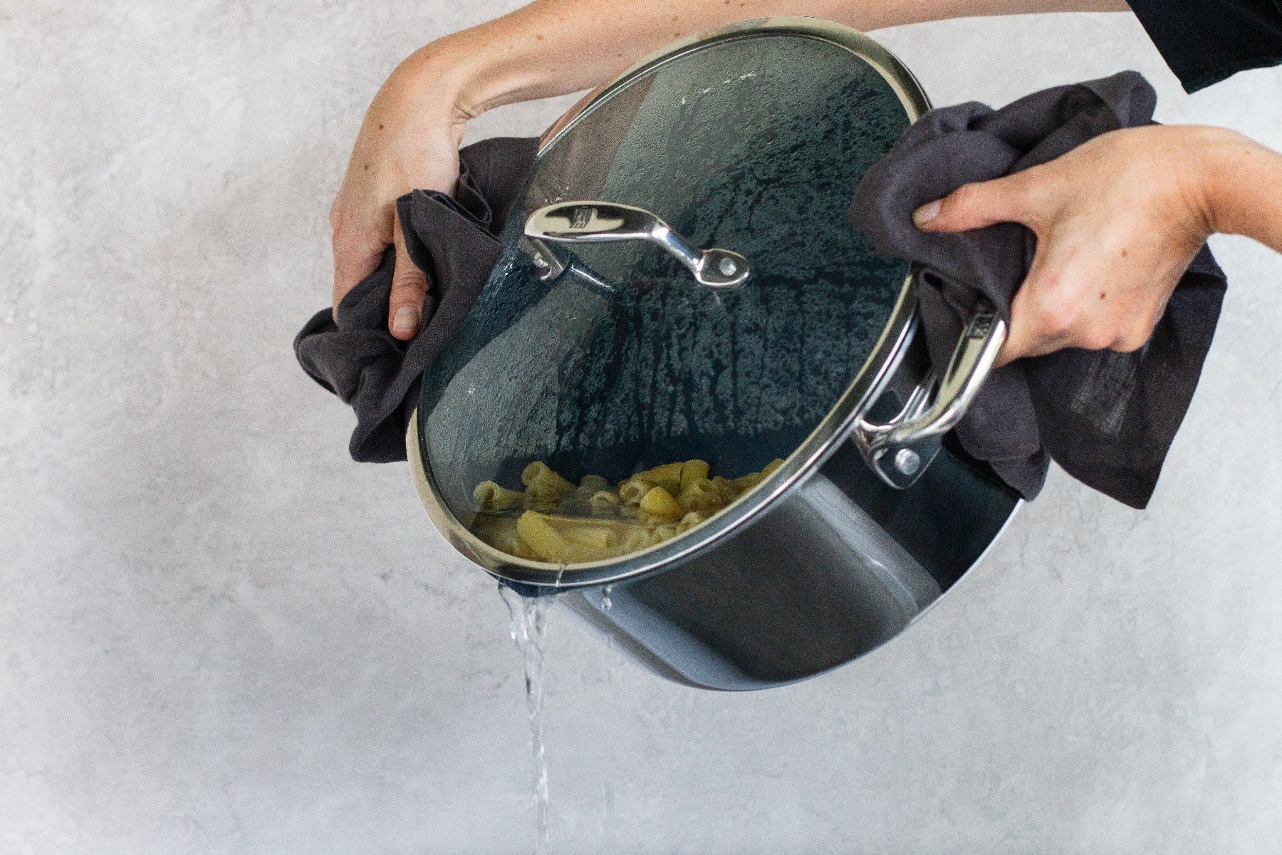 A person straining pasta water from a Zwilling Clad Ceramic CFX 6 qt Dutch Oven. 