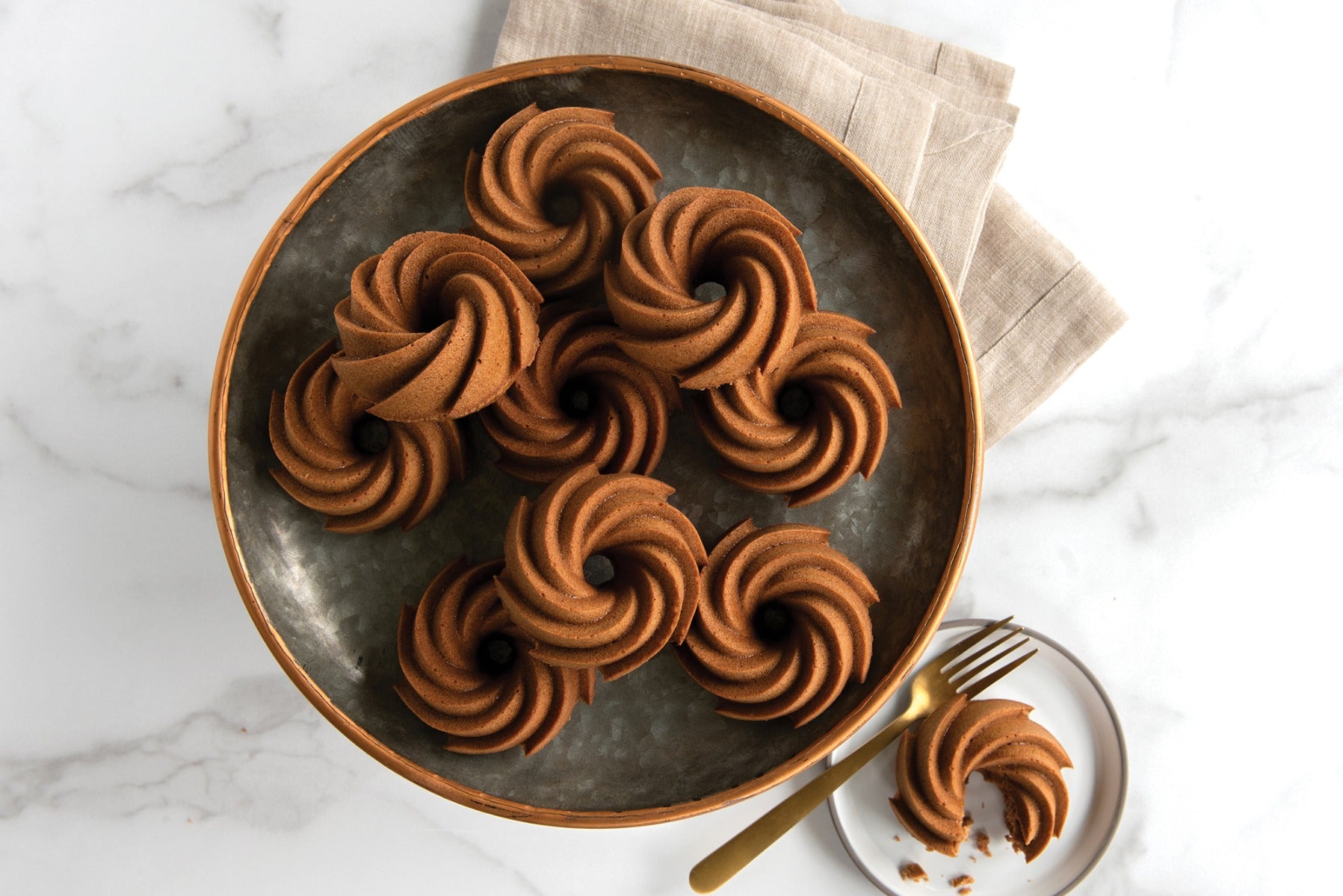 Plate of chocolate swirl cupcakes on marble background with gold fork