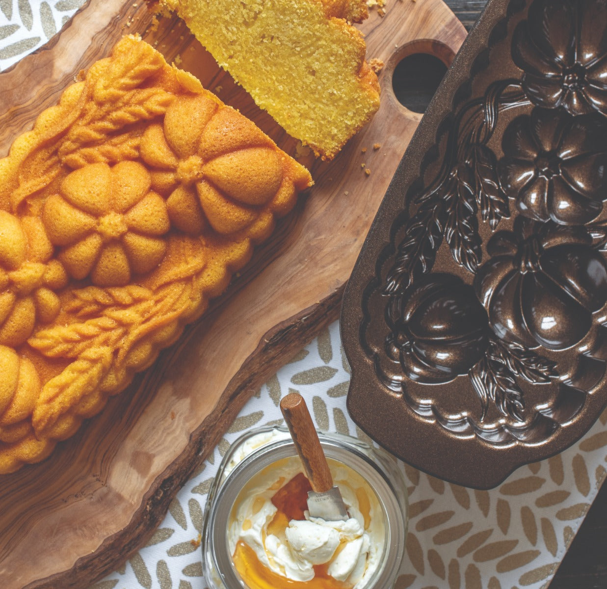 Freshly baked pumpkin-shaped pound cake beside empty bundt pan and whipped cream