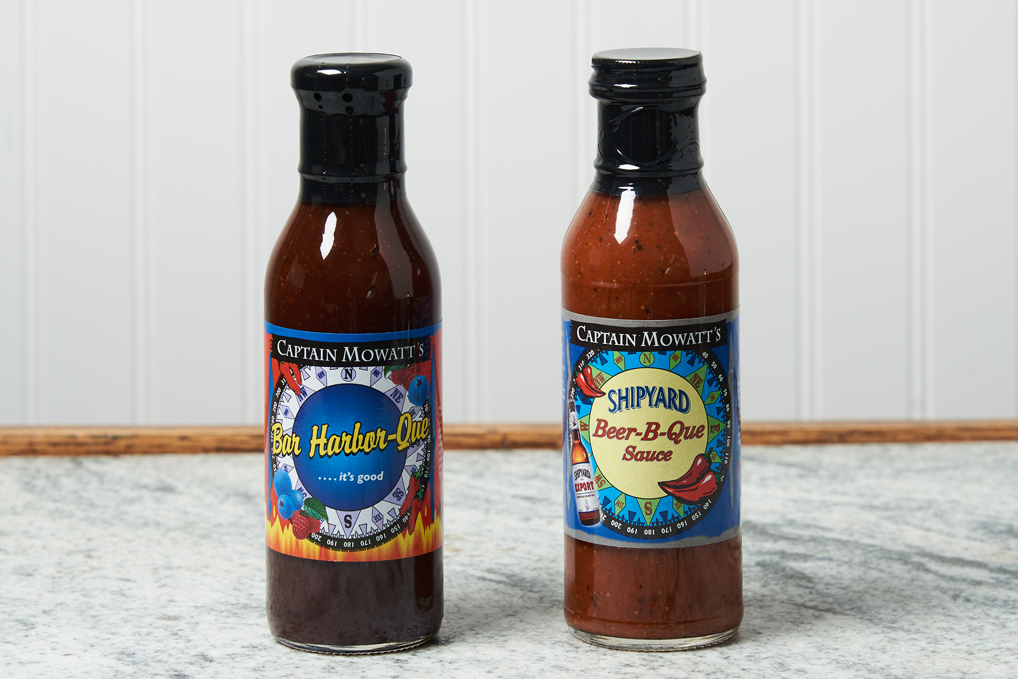 Two bottles of Captain Mowatt's BBQ Sauce sits on a marble countertop. The flavors are Bar Harbor-Que and
Shipyard Beer-B-Que.
