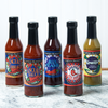 An assortment of Captain Mowatt's Hot Sauce sits on a marble countertop. The flavors include: Blue Flame, Greenie, Canceaux Sauce, Canceaux Turbeaux, and Boston Red Sauce.
